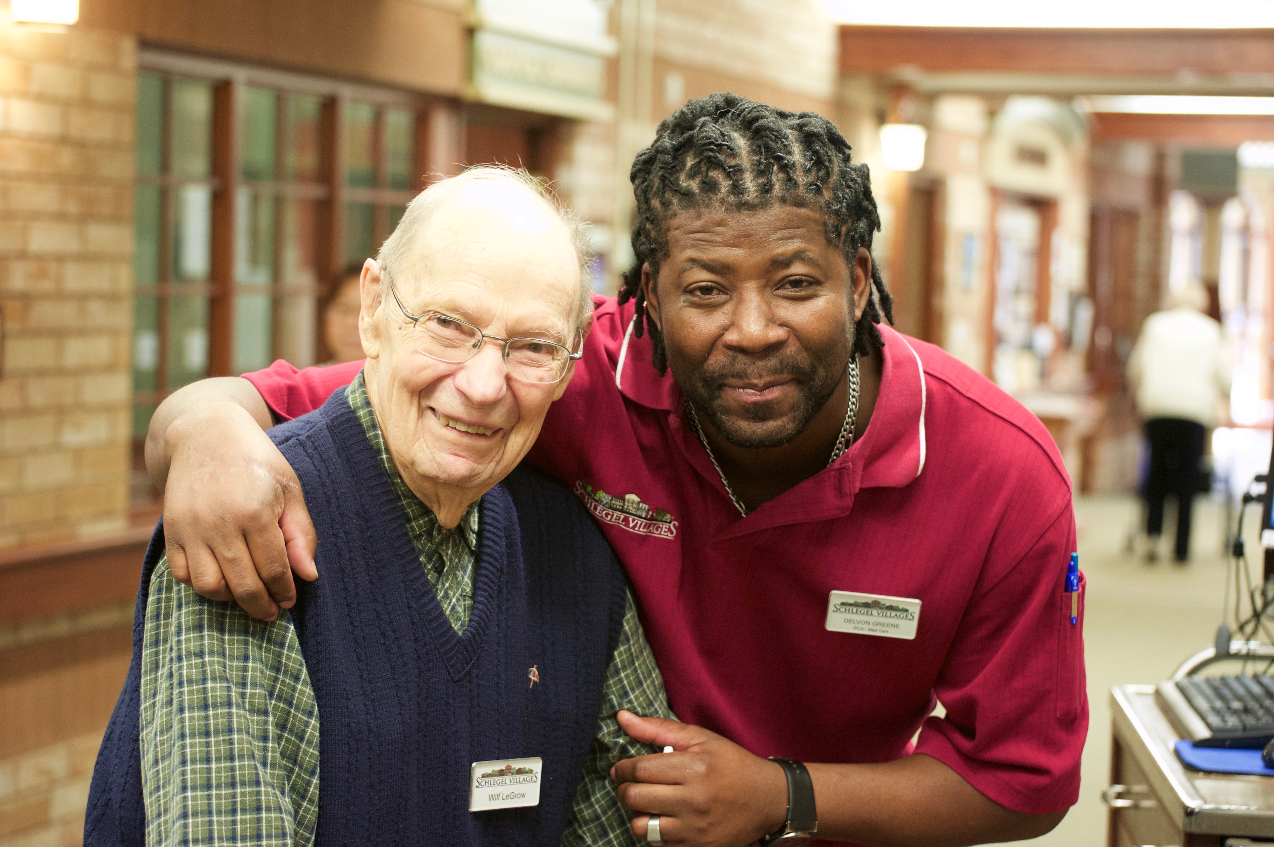 Schlegel Villages team member poses with senior man for a photo on main street at the village