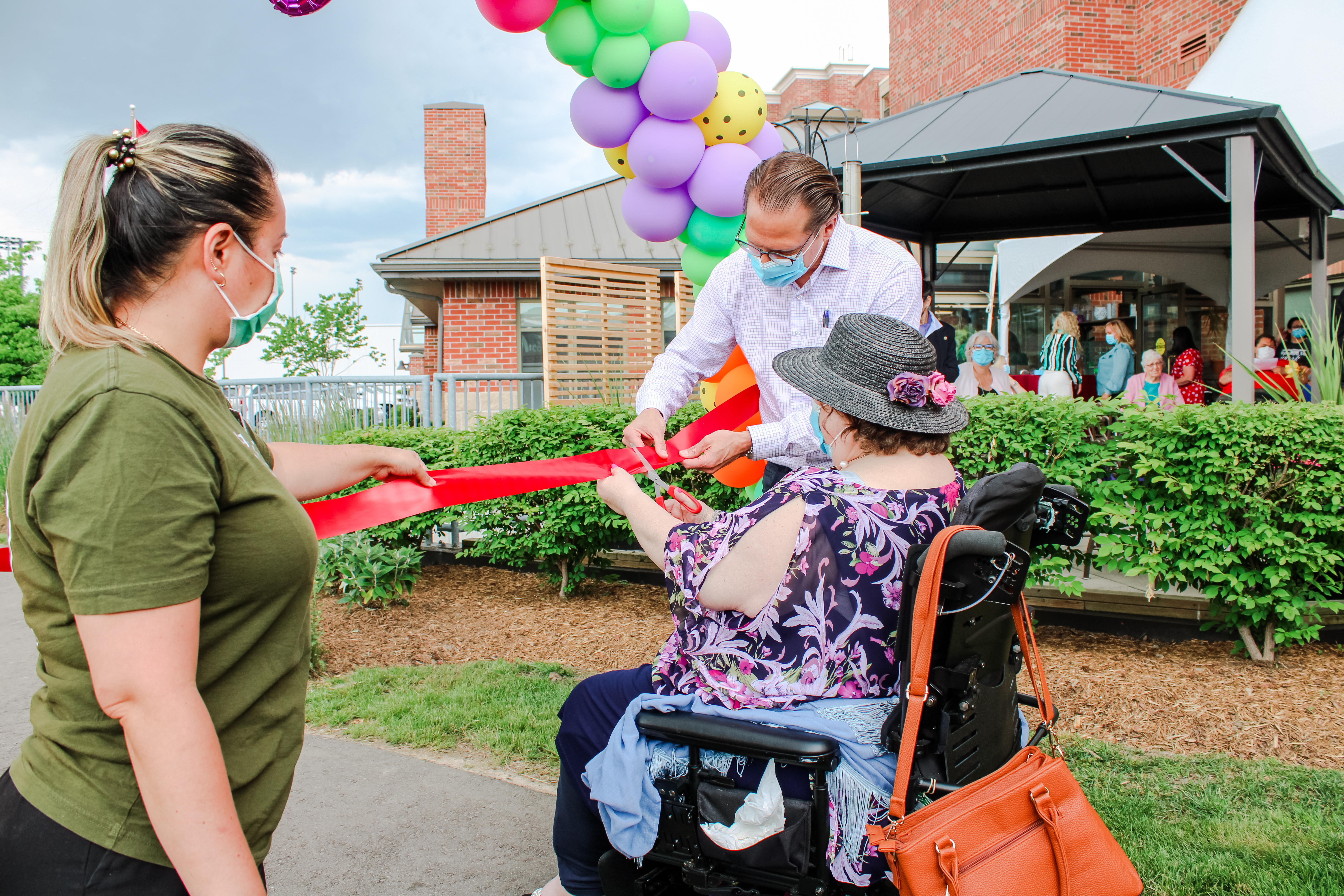 Resident cutting the ribbon for the opening of the Healing Garden with a team member and Jamie Schlegel